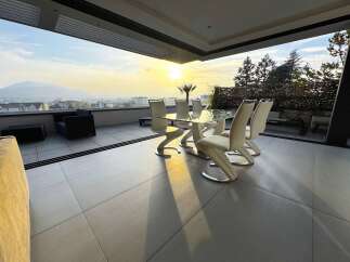 Enjoy breathtaking sunset views from this modern patio, featuring a sleek glass-top dining table and comfortable seating.