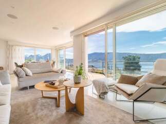 Experience breathtaking panoramic views from this stunning living room, featuring floor-to-ceiling windows that showcase a serene lake and majestic mountains.