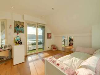 This charming attic bedroom offers a serene retreat with stunning natural light streaming through large sliding glass doors.