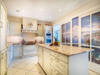 Experience luxury in this stunning kitchen featuring custom cream cabinetry with ornate detailing and a spacious granite-topped island perfect for entertaining.