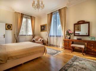 Experience elegant living in this beautifully appointed bedroom, featuring a plush bed, ornate furnishings, and a charming armchair.