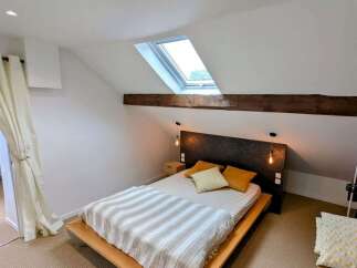 Discover this charming attic bedroom featuring a comfortable bed with a stylish striped duvet and a unique headboard.