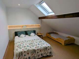Discover this charming attic bedroom featuring a comfortable double bed with a floral duvet and a unique built-in headboard with ambient lighting.
