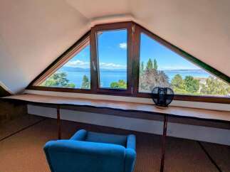 Enjoy breathtaking lake views from this unique attic room, featuring a custom live-edge desk and a comfortable blue armchair.