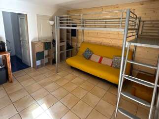Discover this charming studio apartment featuring a space-saving loft bed and a vibrant yellow sofa, perfect for maximizing living space.