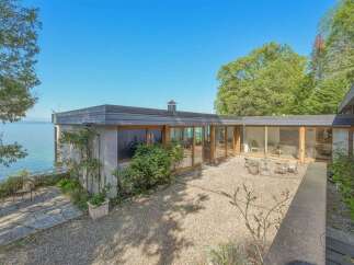 Experience breathtaking lakefront living in this stunning modern home, featuring expansive glass walls that seamlessly blend indoor and outdoor spaces.