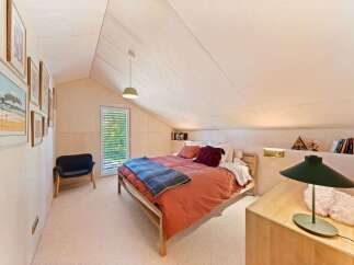 Discover this charming attic bedroom, featuring a cozy bed with a burnt orange duvet and a blue plaid throw.