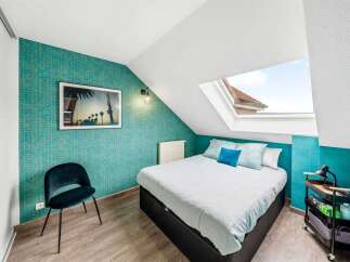 Discover this charming attic bedroom featuring vibrant teal wallpaper and a large skylight that floods the space with natural light.
