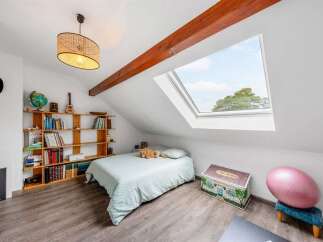 Discover this charming attic bedroom, bathed in natural light from a large skylight offering picturesque views of the sky and trees.