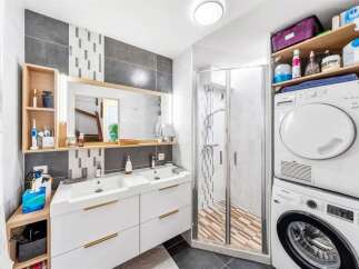 This modern bathroom features a double vanity with ample storage and sleek gold hardware, complemented by a stylish tiled accent wall.