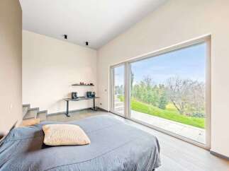 Experience modern living in this stunning bedroom featuring a large, floor-to-ceiling window that floods the space with natural light and offers breathtaking views of the lush green landscape.