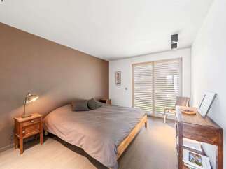 This modern bedroom features a comfortable king-size bed with plush grey bedding, complemented by a warm brown accent wall.