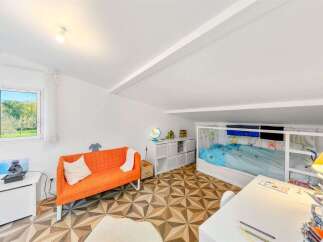 This charming attic bedroom features a vibrant orange sofa, a loft bed with blue bedding, and a dedicated study area with a white desk.