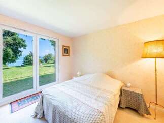 Experience serene living with this charming bedroom featuring a large sliding glass door that opens to breathtaking lake views and lush greenery.