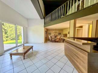 Experience spacious living in this open-concept home featuring a large living area with a coffee table and expansive windows overlooking lush greenery.