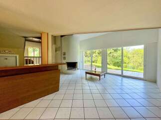 Experience modern living in this spacious room featuring a striking cylindrical fireplace and a large wooden bar.