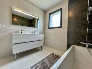 This modern bathroom features a sleek double vanity with chrome faucets, complemented by a large illuminated mirror.