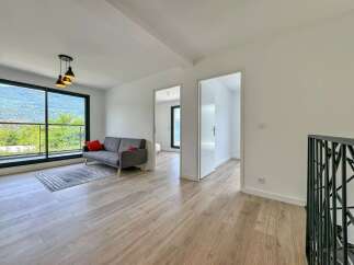 Experience modern living in this spacious apartment featuring a comfortable grey sofa with red accent pillows, complemented by a stylish rug and light wood flooring.