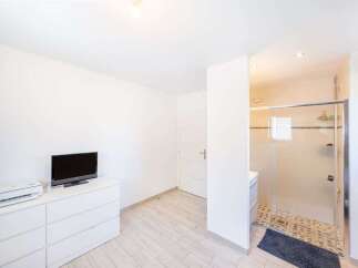 This modern bedroom features a sleek white dresser topped with a flat-screen TV and a printer, offering convenient entertainment and workspace.