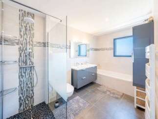 This modern bathroom features a sleek grey double vanity with ample storage, complemented by a spacious walk-in shower with decorative tile accents.