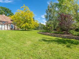 Experience serene living in this beautiful property featuring a charming house with a sunroom, surrounded by lush green lawns and mature trees.