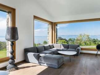 Experience breathtaking panoramic views from this modern living room, featuring expansive windows that frame a stunning waterscape and lush greenery.