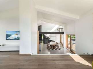This modern open-concept living space features a striking multi-level design with a sleek black metal beam supporting an upper walkway.