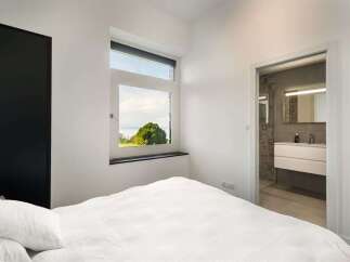 Experience serene living in this modern bedroom featuring a large window with breathtaking views of lush greenery and water.