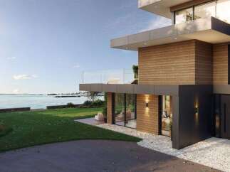 Experience luxury living in this modern waterfront home, featuring expansive glass windows and a sleek wooden exterior.