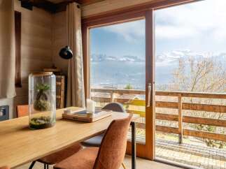 Experience breathtaking mountain views from this charming dining area, featuring a large glass terrarium and a wooden table set for intimate meals.