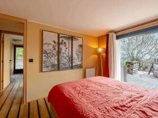 Experience tropical tranquility in this inviting bedroom, featuring a vibrant red comforter and striking triptych wall art depicting lush palm trees.