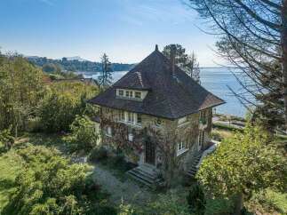 Discover this charming stone house with a distinctive pitched roof, nestled amidst lush greenery and offering stunning water views.
