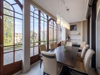 Experience elegant dining in this sun-drenched room, featuring a large wooden table surrounded by plush upholstered chairs.