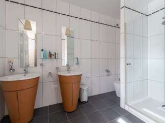 This modern bathroom features dual pedestal sinks with wooden bases, offering ample space for morning routines.
