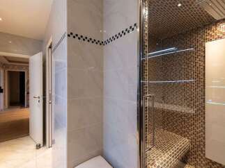 Experience luxury in this modern bathroom featuring a stunning mosaic-tiled shower enclosure with a built-in bench and sleek glass shelves.