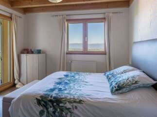 Experience breathtaking views from this serene bedroom, featuring a comfortable bed with floral bedding and a large window overlooking a picturesque landscape.