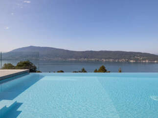 Experience luxury living with this stunning infinity pool offering breathtaking panoramic views of the serene lake and majestic mountains.