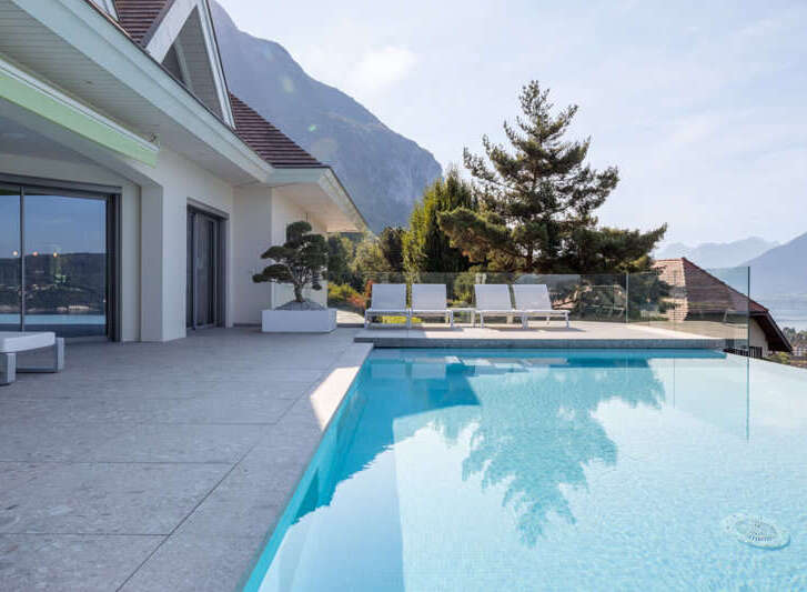 Experience luxury living with this stunning infinity pool overlooking a serene lake and majestic mountains.