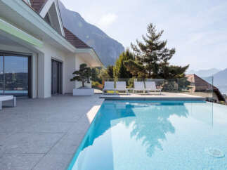 Experience luxury living with this stunning infinity pool overlooking a serene lake and majestic mountains.