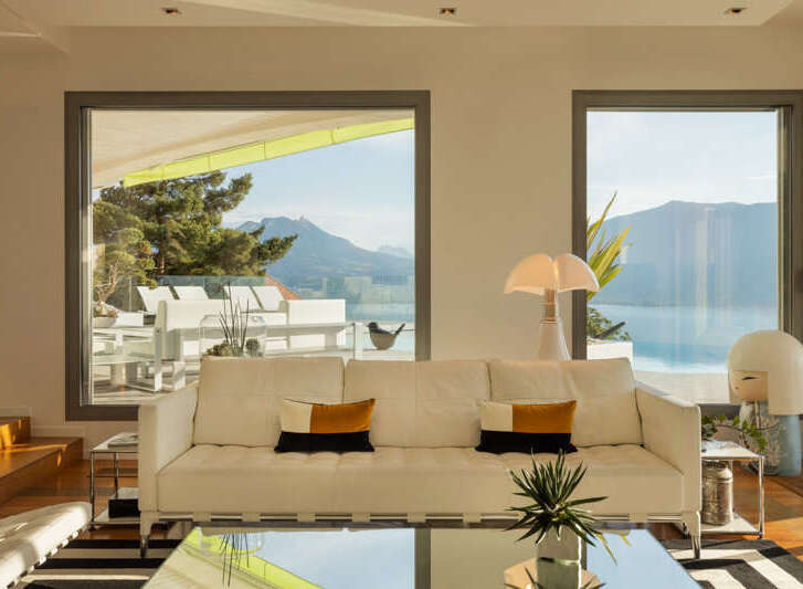 Experience breathtaking panoramic views from this stunning living room, featuring expansive windows that frame a majestic mountain and lake landscape.