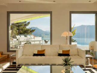 Experience breathtaking panoramic views from this stunning living room, featuring expansive windows that frame a majestic mountain and lake landscape.