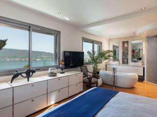 Experience luxury living in this stunning bedroom with breathtaking lake and mountain views through expansive windows.