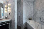 Experience luxury in this marble-clad bathroom featuring a sleek vanity with modern lighting and a spacious soaking tub.