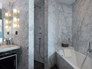 Experience luxury in this marble-clad bathroom featuring a sleek vanity with modern lighting and a spacious soaking tub.
