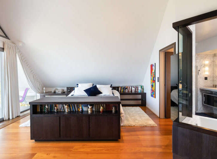 This spacious bedroom features a built-in dark wood bookcase that spans the width of the bed, offering ample storage for books and decor.