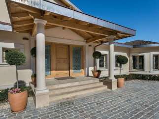 This elegant home features a grand entrance with double wooden doors, flanked by classical columns and a covered porch.