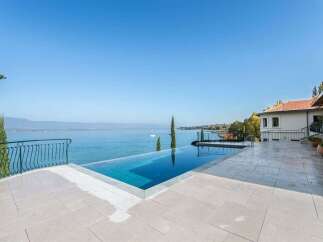 Experience luxury living with this stunning infinity pool overlooking a serene lake and distant mountains.
