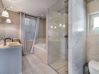 This modern bathroom features a spacious walk-in shower with elegant marble tiling and a separate bathtub.