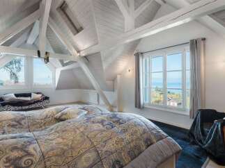 Experience breathtaking lake views from this charming attic bedroom, featuring exposed white beams and a large picture window.