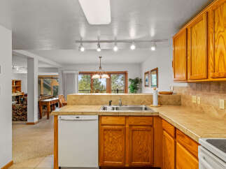 This spacious kitchen features warm oak cabinetry and a tiled backsplash, complemented by a double basin sink and a white dishwasher.